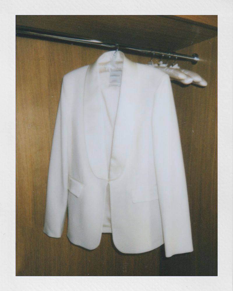 Ivory-colored blazer hangs in a wood closet with a white hanger. The blazer is lightweight and hangs neatly on the hanger.