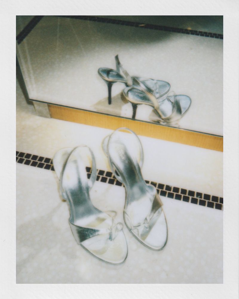 Elegant silver high-heeled shoes are captured in a sophisticated still life, positioned on a marble tile surface with reflection.