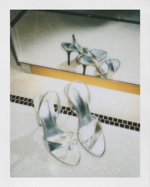 Elegant silver high-heeled shoes are captured in a sophisticated still life, positioned on a marble tile surface with reflection.