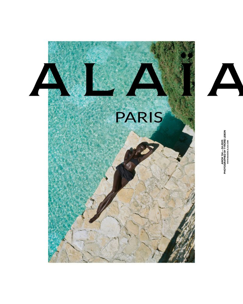 Fashion ad featuring a dark-skinned woman in swimwear, lying on stone near a pool, with 'ALAIA PARIS' text, shot in natural light.