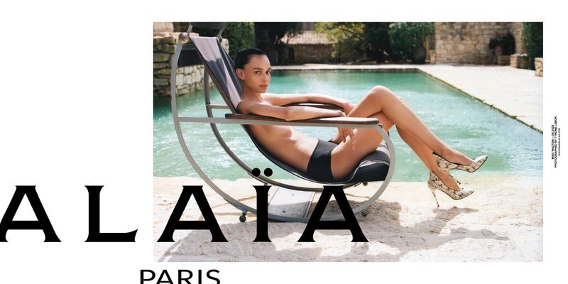 A woman lounges by a pool in high heels for an Alaïa Paris ad, captured in an eye-level medium shot under natural lighting. 