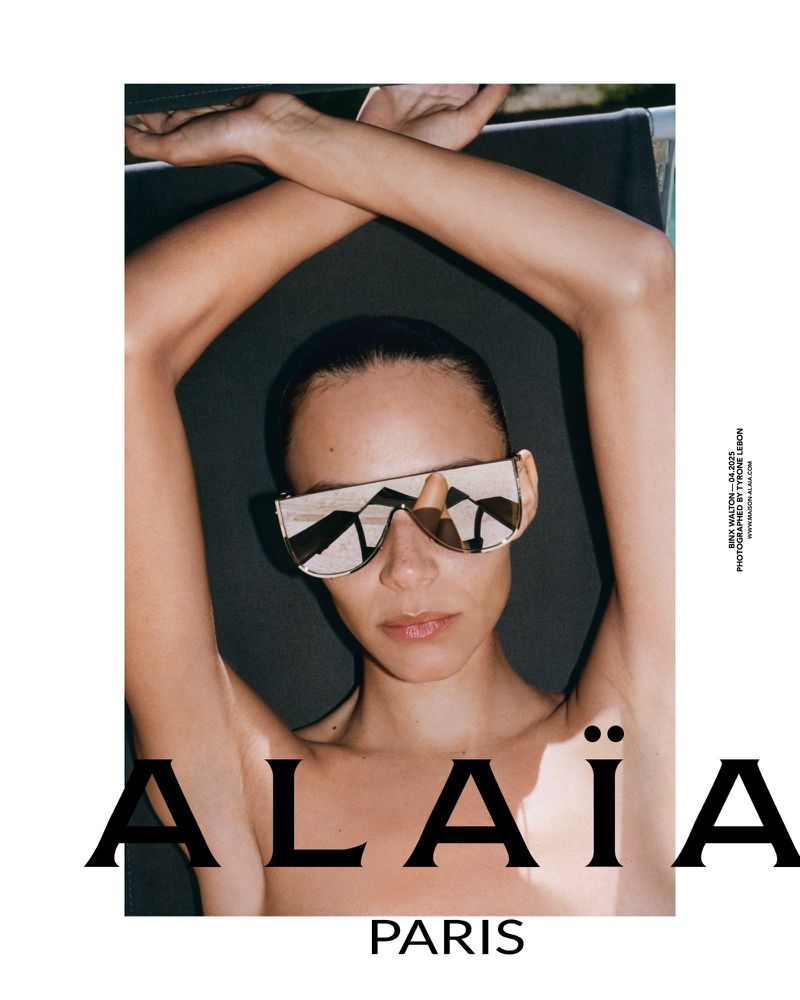 A woman wearing designer sunglasses poses outdoors with her arms crossed above her head. Fashion shot for an ad campaign.