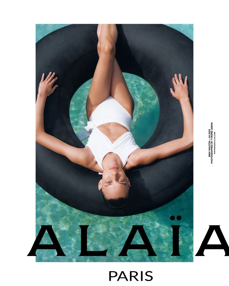 Woman in white swimsuit floats in black inner tube in bright turquoise water, an overhead angle for fashion editorial.