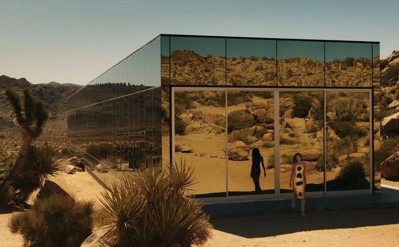 Adult female in a patterned dress walks in front of a modern, mirrored building in the desert landscape on a sunny day.