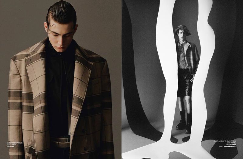 Editorial fashion shot: A male model in a plaid blazer and black shirt poses in a studio with monochromatic backgrounds and paper cutouts.