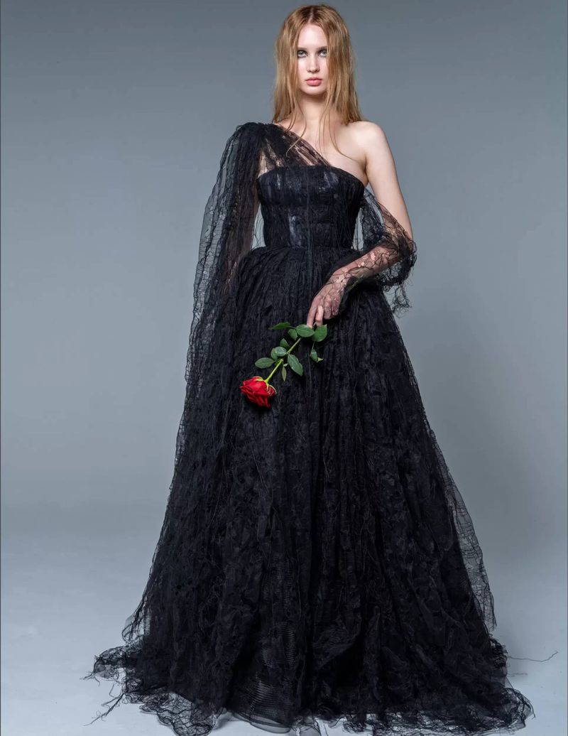 Elegant woman poses in a dark lace gown with a red rose against a gray background in a studio fashion editorial photography shot.