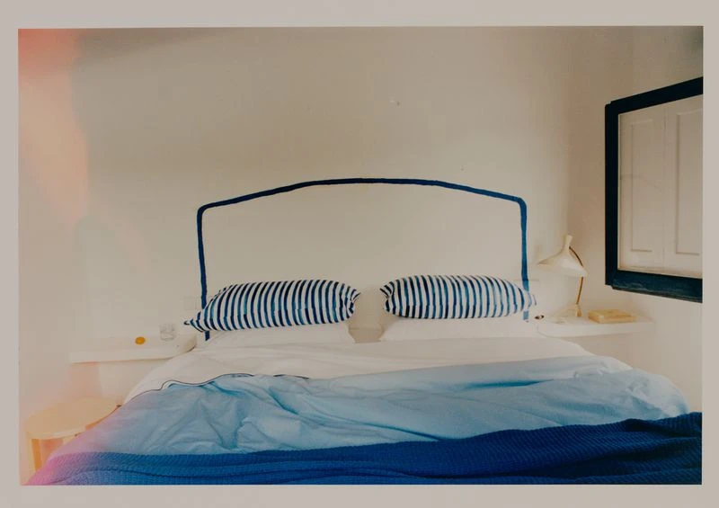 Bedroom interior featuring a bed with blue striped pillows and a blue gradient blanket, white walls, minimalist decor, and a window.