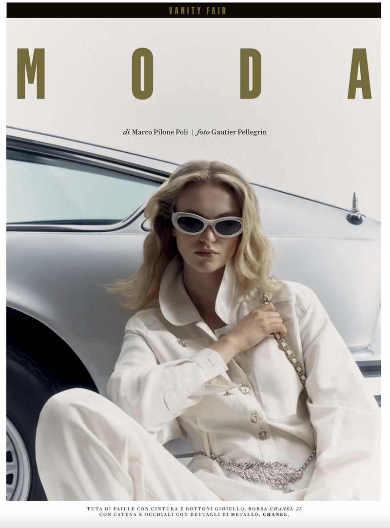 Fashion editorial featuring a fair-skinned blonde woman in a white outfit and sunglasses, posing beside a vintage car for Vanity Fair magazine.
