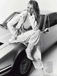 Model leaning on a vintage car wearing a white jacket and trousers against a white backdrop