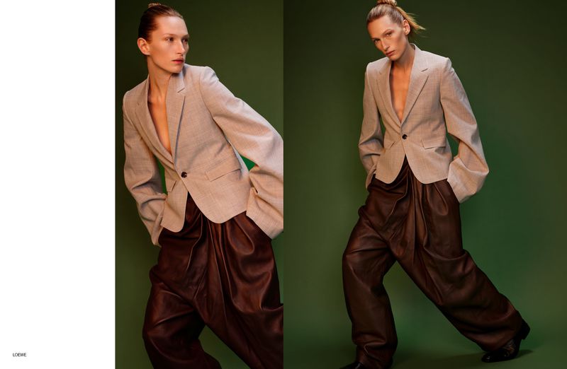 Fashion shot of a woman in a beige blazer and brown leather pants posing against a green backdrop, showcasing a contemporary style.