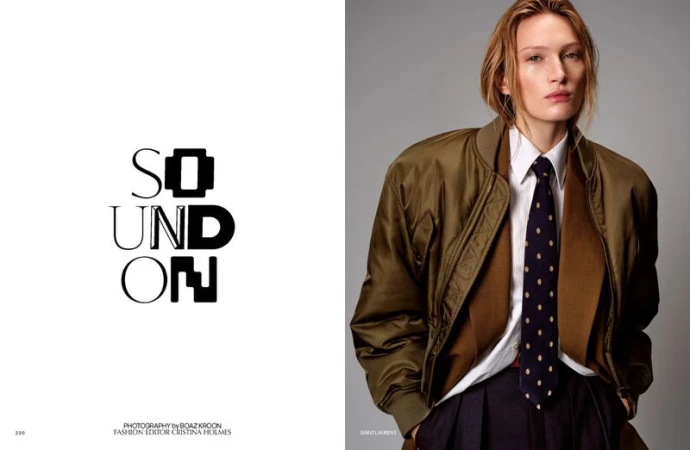 Fashion editorial portrait of an adult woman wearing an olive bomber jacket, white shirt, and navy tie in a photo studio.