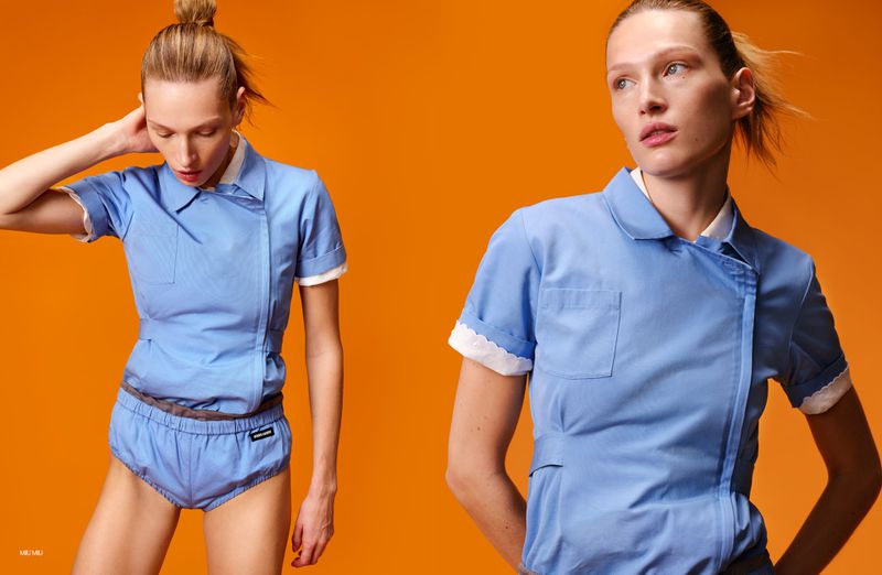 Two adult females in matching blue outfits pose against an orange backdrop, showcasing a fashion editorial with a minimalist aesthetic.