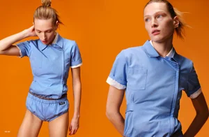 Model Liz Kennedy in a blue uniform and shorts against a vibrant orange background for At Large Magazine