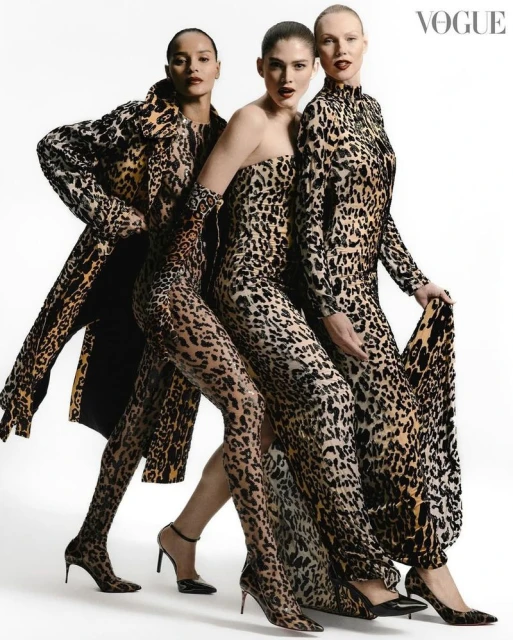 Three fashion models pose in a studio wearing head-to-toe matching leopard print dresses and a coat in front of a white background.