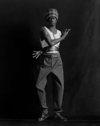 Monochrome fashion portrait of a Black male model wearing a tank top and wide-leg trousers against a dark backdrop