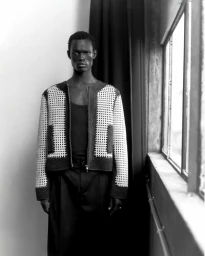 Black man wearing a patterned knit zip-up jacket standing near a large window for GQ Portugal
