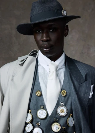Stylish portrait of an adult male wearing a hat and suit vest covered in pocket watches in a photo studio setting.