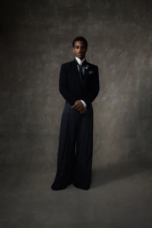 Portrait of an adult male in formal attire standing against a textured grey backdrop in a studio setting, lit with diffused lighting.