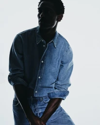 Model Hamid Onifade wearing a denim shirt and jeans against a bright white background for Zara.