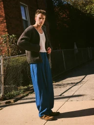 Drew Starkey wearing a dark cardigan and blue trousers outdoors by a brick building for Esquire Australia.