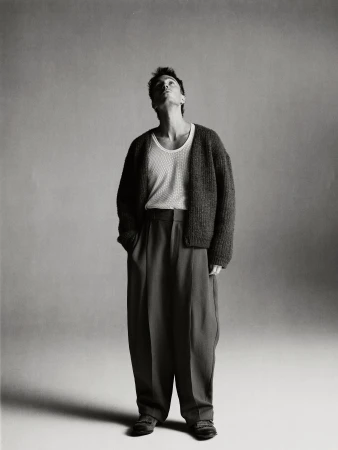 Drew Starkey standing in a knitted cardigan and trousers against a neutral background for Esquire Australia.