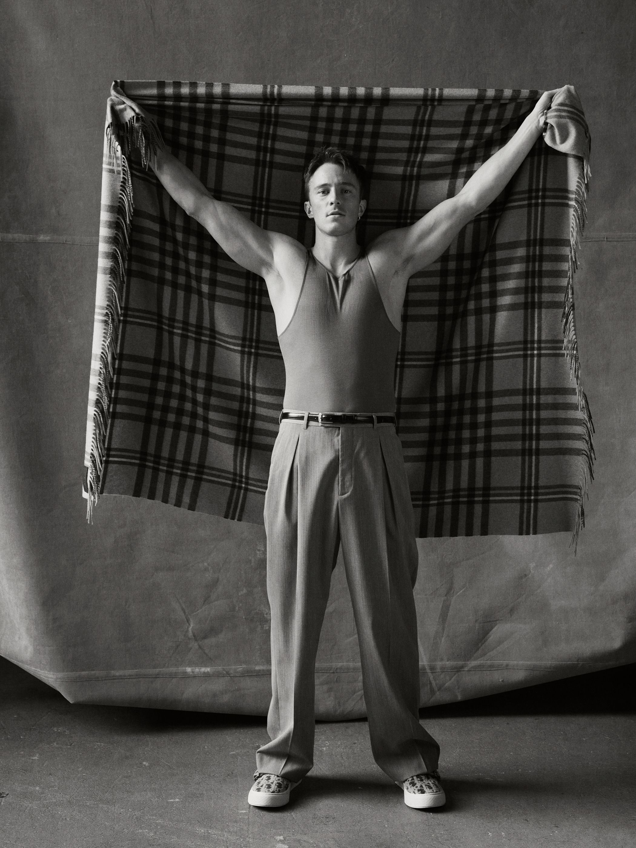 Monochrome portrait of a muscular man in retro athletic wear holding a plaid blanket, studio background, vintage athletic fashion concept.