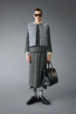 Man poses in grey tweed skirt suit with vest, white collared shirt, dark sunglasses, black dress shoes, socks and black leather doctor's bag.