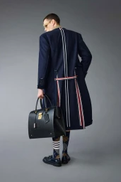 Model wearing a navy coat with white stripes holding a large black leather handbag against a grey background