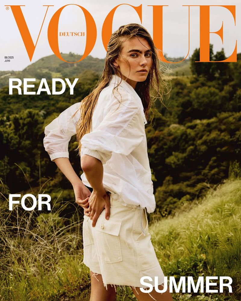 Vogue Deutsch cover featuring a woman in a white shirt and shorts standing in a field with a hilly, green landscape in the background.