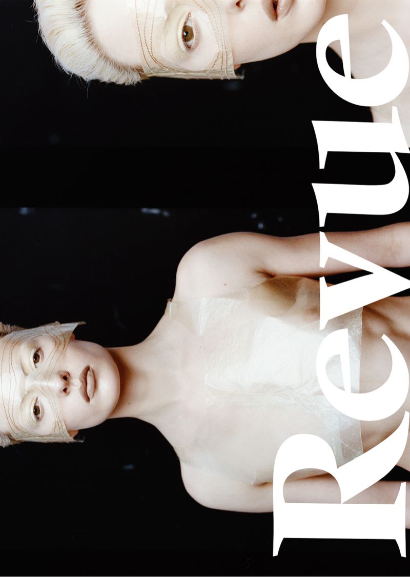 Two women with pale skin and masks are featured in a studio portrait against a black background. The word 'Revue' is written in white text.