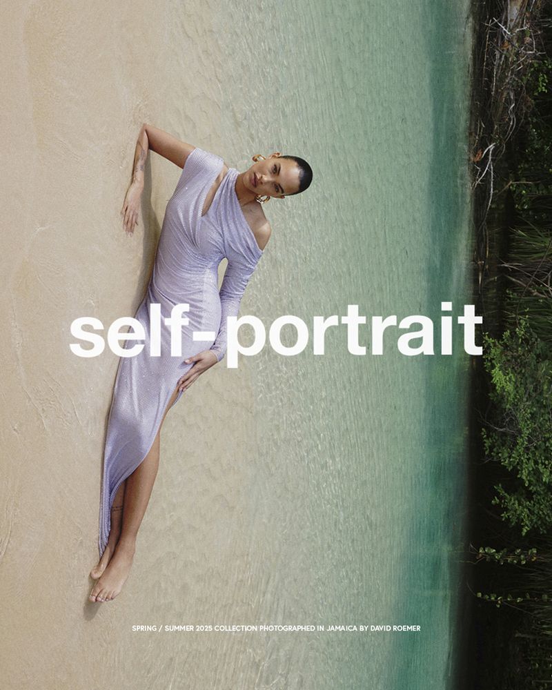Woman in lilac dress poses on sandy beach with clear turquoise water and lush greenery in the background in a fashion editorial.