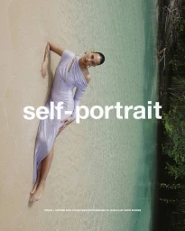 Model lying on sandy beach wearing a lavender dress by the water edge