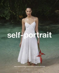 Model standing in crystal clear water wearing a white eyelet dress holding a red flower for Self-Portrait