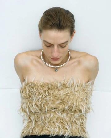 Woman in furry tan top and silver choker poses against a white background, looking down in a fashion studio shot with soft lighting.