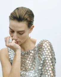 Model wearing a metallic mesh top and silver jewellery with hair slicked back against a clean white background