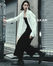 Model wearing a white shirt and black trousers stepping past metal shutter doors outdoors