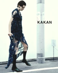 Model in a dark knit dress and black socks walking near a street pole for KAKAN SS25