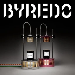 Two Byredo scented candles placed inside industrial mechanical lamp stands against a dark grey background with bold white branding.