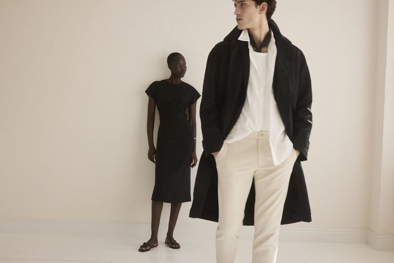 Two fashion models posing in an indoor photo studio with beige backdrop, wearing stylish modern clothing, including a black coat.
