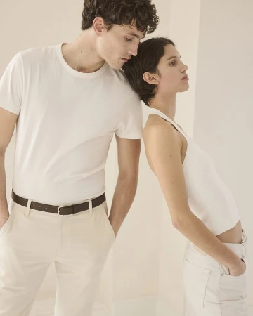 A stylish couple in a photo studio setting, wearing casual white tops and light pants, exhibiting minimalist fashion and studio lighting.