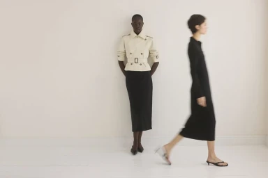 Two models showcasing Club Monaco spring apparel against a plain white studio wall, with one person in motion blur walking past.