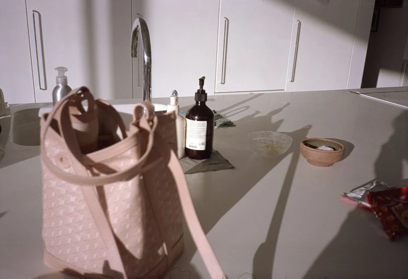 Light pink tote bag on a white countertop with a sink, bottles, and bowls, casting long shadows in a bright indoor kitchen setting.
