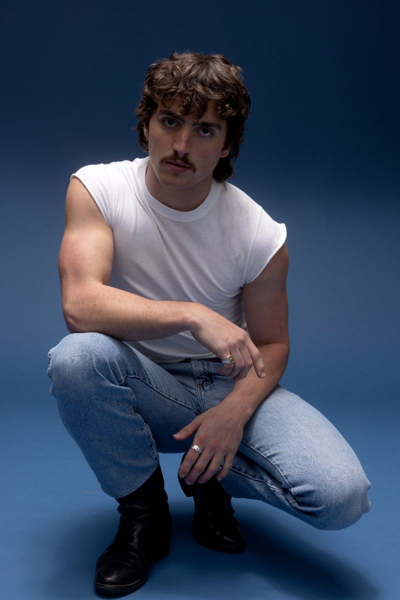 Man in white tee and jeans poses in a studio against blue backdrop, showcasing fashion and portrait photography with casual style.