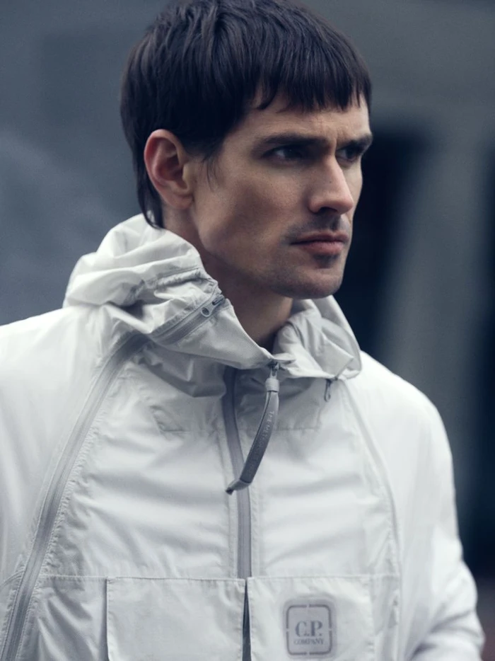 Man wearing a white hooded technical jacket with front pockets against an urban background