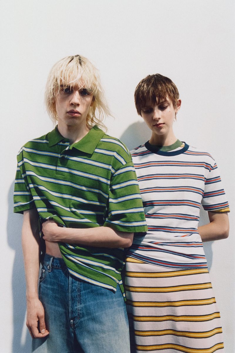 Two models, a man and a woman, pose in a studio setting wearing striped shirts and fashionable jeans and a skirt, creating a clean fashion shot.