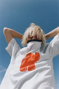 Model wearing a white t-shirt with a red graphic under a clear blue sky