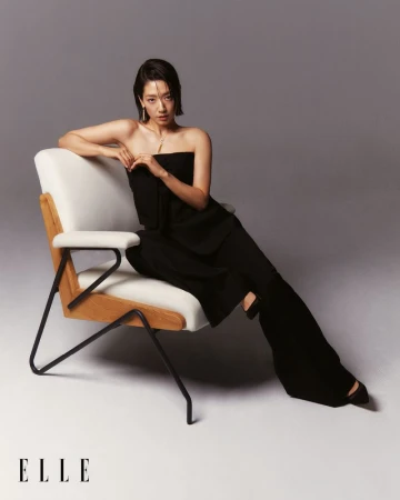 Woman in a black strapless top and wide-leg pants posing in a studio sitting on a chair for a fashion editorial photo shoot.