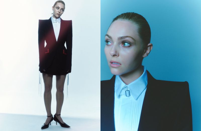 Young woman poses in an oversized black blazer dress with a white shirt. Fashion shot features studio lighting and soft blue backdrop.