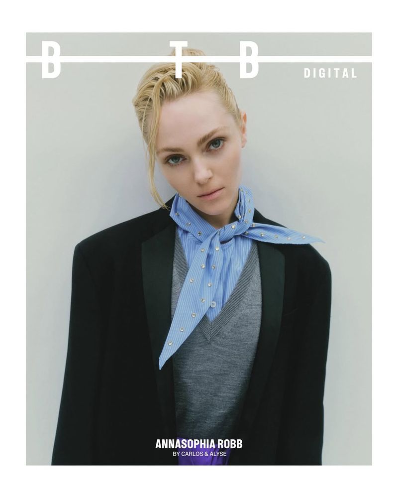 Headshot of Annasophia Robb wearing a black blazer, gray sweater, and blue patterned scarf against a neutral background for BTBD Digital.