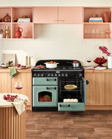 Kitchen interior with a green Falcon range oven and a variety of food items, including a pie, meat, vegetables, and bread rolls.